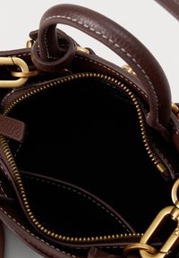 Interno di una borsa a tracolla in pelle marrone con chiusura a cerniera, caratterizzata da una cerniera dorata e dettagli in catena. Texture liscia e design pulito.