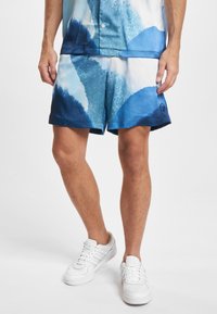 Pánské plavky ve světle modrém a bílém abstraktním vzoru, vyrobené z lehké látky. Mají elastický pas a boční kapsy s rozparkem.