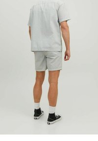 Camisa de manga corta con cuello en gris claro con un patrón texturizado, combinada con pantalones cortos a juego. Unos zapatos deportivos negros de caña alta completan el atuendo.
