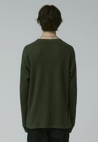 Green long-sleeve top with a waffle texture, rounded neckline, and dropped shoulders. Simple design, suitable for casual wear.