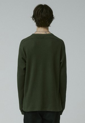 Green long-sleeve top with a waffle texture, rounded neckline, and dropped shoulders. Simple design, suitable for casual wear.