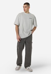 Svijetlosivi oversized majica kratkih rukava s malim crnim logom. Uparena s tamnosivim širokim trapericama i sivim tenisicama.