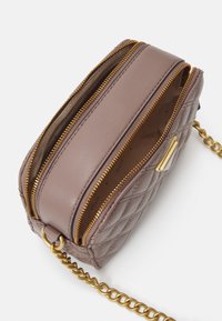 Mała lawendowa skórzana torebka na ramię z pikowanym wzorem, z dwoma otwartymi złotymi suwakami i złotym łańcuszkiem na białym tle.