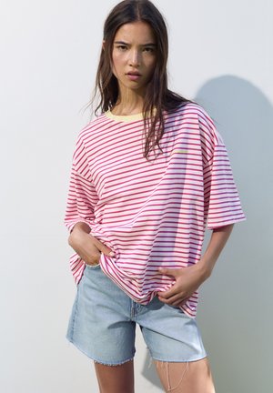 T-shirt rayé en rose et blanc avec un col jaune, associé à un short en denim aux bords effilochés, créant un look décontracté et décontracté.