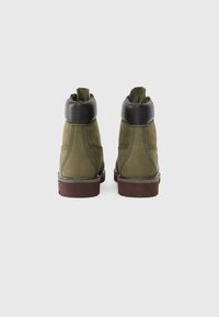 Botas de ante verdes con un collar de cuero negro, que cuentan con una suela resistente, detalles de costura y un tobillo acolchado para mayor comodidad.