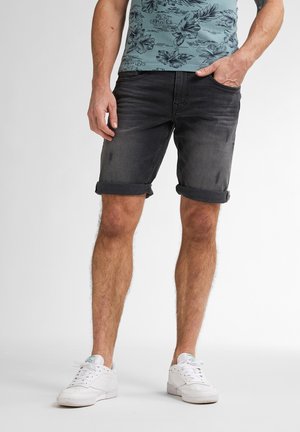 Sorte denimshorts med opfoldede kanter, som har en let falming og diskrete slid. Parret med en mønstret blå kortærmet skjorte og hvide sneakers.