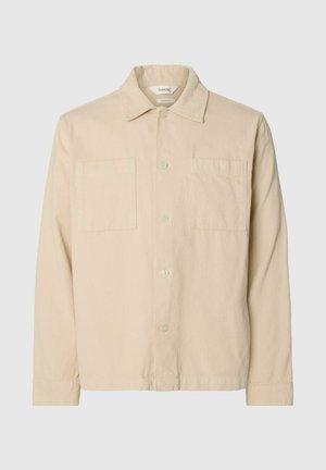 Camisa chaqueta de pana beige con mangas largas, dos bolsillos en el pecho, cierre de botones y cuello clásico sobre un fondo gris claro.