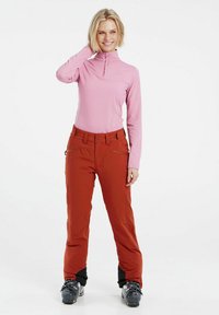 Top a maniche lunghe rosa con zip e pantaloni da sci arancioni con tasche, abbinati a stivali da neve neri. Tessuto morbido e vestibilità su misura.