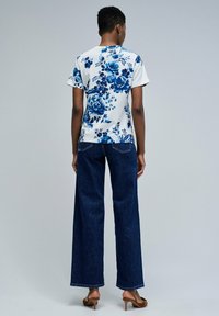 Camiseta de estampado floral en azul y blanco, combinada con jeans de mezclilla oscuros de pierna ancha. El modelo lleva sandalias de tacón marrones.