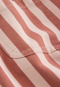 Primo piano di un tessuto con strisce verticali alternate di rosa acceso e rosa chiaro e cuciture visibili lungo una cucitura curva.