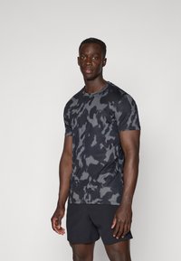 T-shirt de sport à manches courtes en noir avec un motif camouflage gris, fabriqué en tissu léger, doté d'un col rond et d'une coupe ajustée.