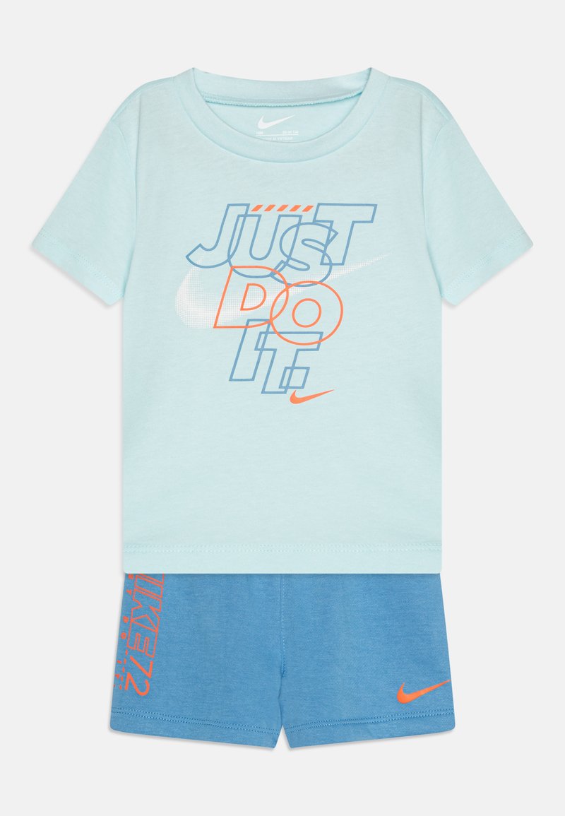 Camiseta azul clara con el gráfico "JUST DO IT" en azul y naranja, combinada con pantalones cortos azules que tienen un logo de Nike naranja en el lateral.
