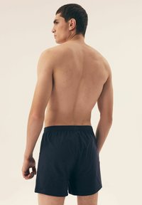 Granatowe kąpielówki z elastycznym paskiem w talii, wykonane z lekkiego materiału, o prostym wzorze i prostym kroju, widok z tyłu.