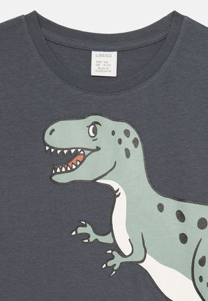 Szürke pamut póló, nagy zöld dinoszaurusz grafikával, fekete foltokkal és részletekkel. Rövid ujjú és kerek nyakú.