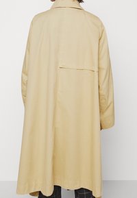 Beige, lättviktig kappa med knappstängning bak, långa ärmar och en lös passform, med en enkel krage och slät yta.