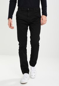 Černé bavlněné kalhoty s rovně střihovým designem, vybavené knoflíkovým zapínáním a poutky na pásek, doplněné o bílé tenisky.