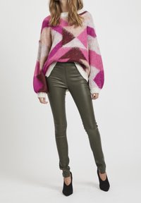 Maglione lavorato a maglia con motivi geometrici rosa, viola e crema; abbinato a pantaloni aderenti verde oliva. Tacchi a punta neri.
