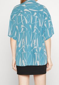 Camicia blu a maniche corte con un motivo astratto bianco, realizzata in tessuto leggero con una vestibilità comoda e un dettaglio sul retro.