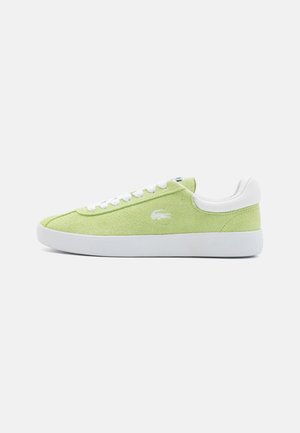 Zapatilla de ante verde con acentos y cordones de cuero blanco. Presenta una puntera redondeada y suela de goma plana. Logo de Lacoste bordado en el lateral.