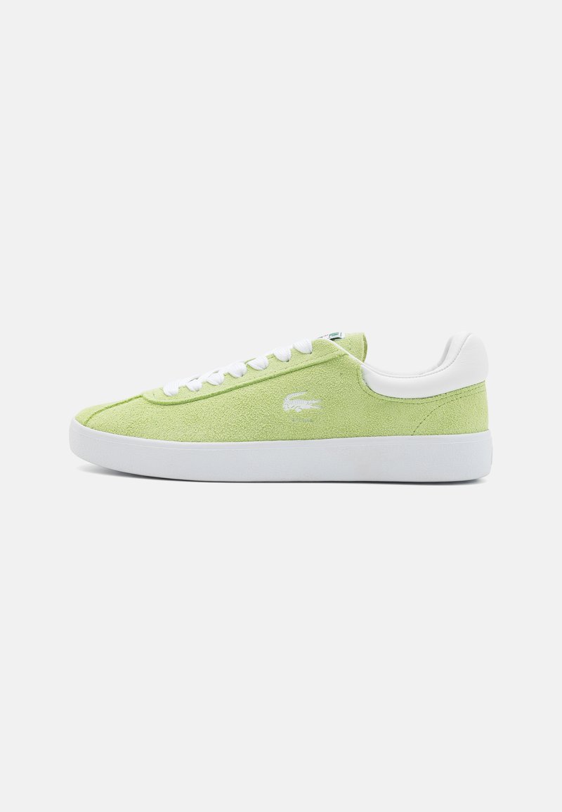Zapatilla de ante verde con acentos y cordones de cuero blanco. Presenta una puntera redondeada y suela de goma plana. Logo de Lacoste bordado en el lateral.