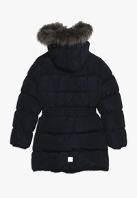 Chaqueta tipo puffer en azul marino con capucha forrada de pelaje, cintura elástica, diseño acolchado y un pequeño logo cuadrado blanco en la parte posterior.