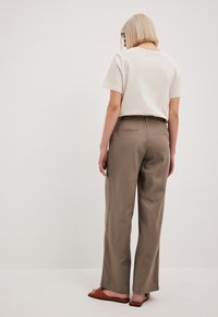 Jasno-beżowa koszulka o luźnym kroju, zestawiona z spodniami o wysokim stanie i szerokimi nogawkami w stonowanym brązowym materiale. Widać brązowe płaskie sandały.