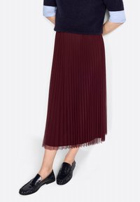 Burgundy pleated skirt with sheer lining, paired with black loafers. Skirt has textured folds and falls mid-calf. Sweater has navy color.