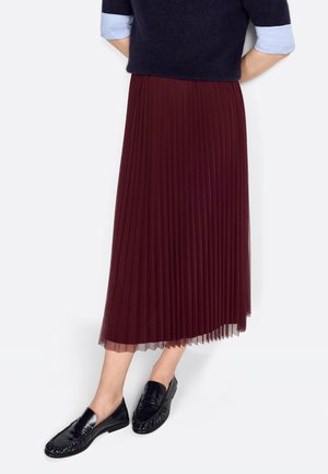 Gonna plissettata bordeaux con fodera trasparente, abbinata a mocassini neri. La gonna presenta pieghe testurizzate e arriva a metà polpaccio. Il pullover è di colore blu navy.