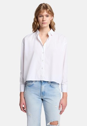 Hvid cropped knap-up skjorte med lange ærmer, klassisk krave, blød tekstur og afslappet pasform, parret med lyseblå slidte jeans.