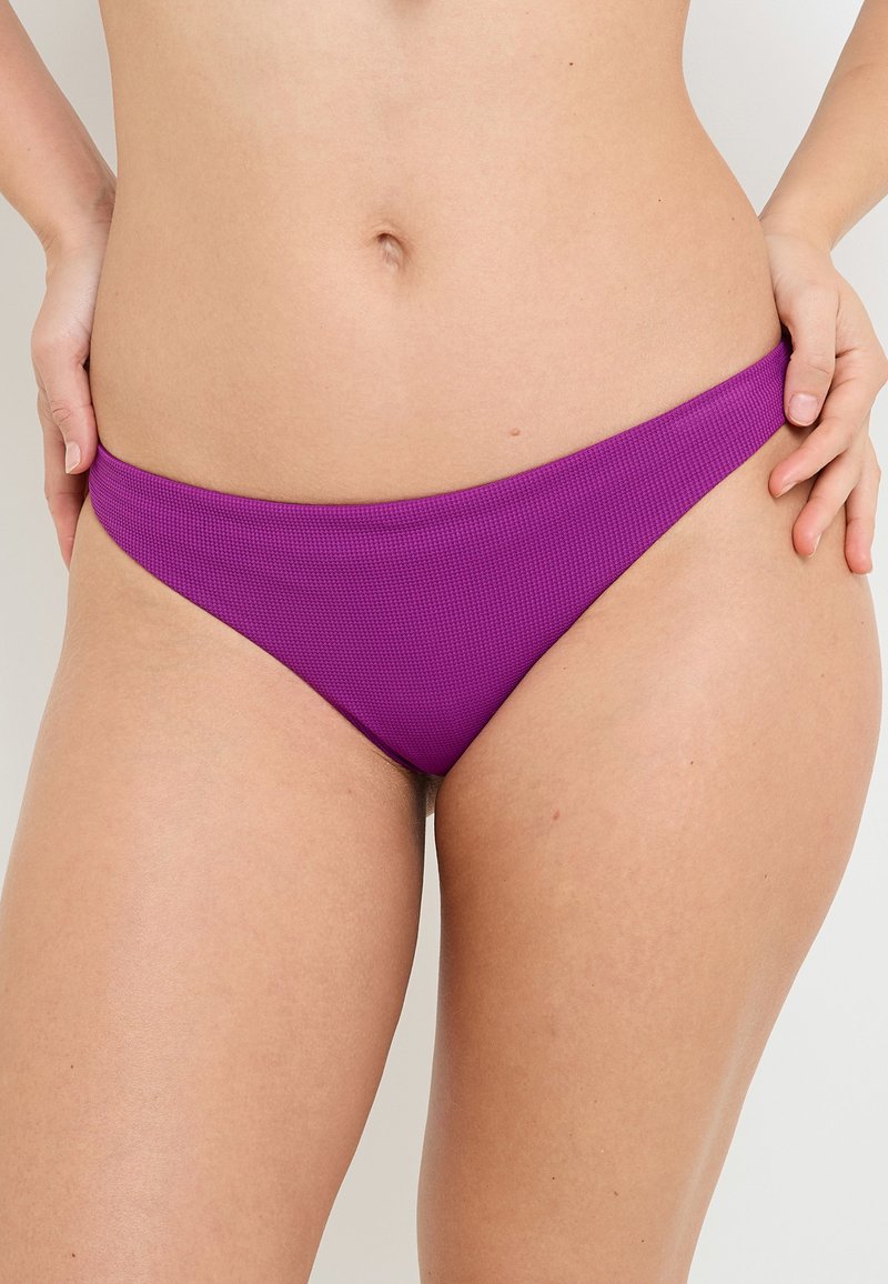 Parte inferiore di bikini viola caratterizzata da un tessuto testurizzato, design a vita bassa e sottili cinturini laterali, che esaltano una silhouette morbida.