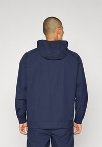 Marineblauwe hoodie met elastische manchetten en zoom, met een zachte textuur en minimalistisch ontwerp. De achteraanzicht benadrukt de schone lijnen.