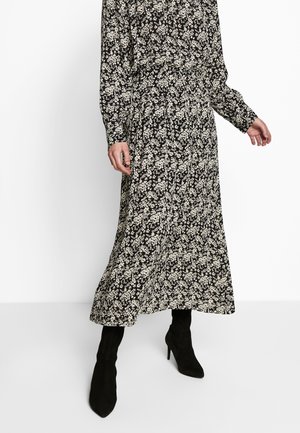 Zwarte bloemenjurk met lange mouwen en een getailleerde taille, voorzien van een patroon van witte bloemen. Gecombineerd met zwarte laarzen met hoge hak.