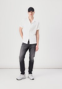Chemise à manches courtes blanche à boutons, jean en denim gris et chaussures de sport blanches. Casquette noire et boucles d'oreilles en tant qu'accessoires notables.