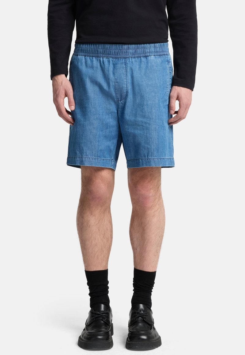 Shorts in denim blu chiaro con vita elastica, taglio dritto e orlo arrotolato. Indossati con calze nere e scarpe.