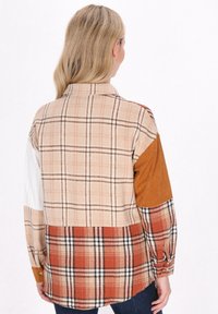 Rutigt skjorta med knappar i kontrasterande tyger i beige, orange och brunt, med långa ärmar och en böjd nederkant. Texturerat material genom hela plagget.