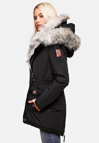 Parka negra con capucha forrada de piel, cintura ajustada, botones a presión, bolsillos laterales y parche con logo en la manga. Textura de tela suave.