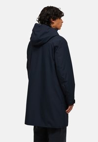 Marineblauwe, waterdichte jack met capuchon en een losse pasvorm. Bevat een middennaad, zijzakken en elastische manchetten voor extra bescherming.