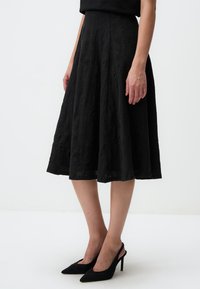 Gonna midi nera con tessuto testurizzato, design svasato e vita liscia. Abbinata a scarpe con tacco a punta nere.