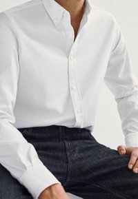 Camicia bianca in cotone con colletto classico, caratterizzata da una texture liscia. Abbinata a jeans in denim scuro con una vestibilità comoda.