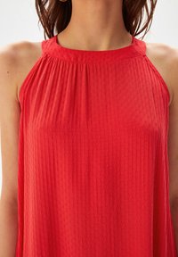 Haut sans manches rouge en tissu texturé avec des rayures horizontales, un col froncé et une silhouette décontractée.