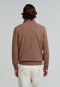 Brun strikket pullover med ståkrave, ribbede manchetter og kant. Blød tekstur, tætsiddende design, passer godt med lyse bukser.