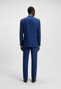 Blauw pak met een tailored fit, voorzien van een enkele split, gestructureerde schouders en een effen voorkant bij de broek. Afgewerkt met elegante zwarte schoenen.