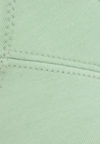 Hellgrüner Stoff mit glatter Textur, der diagonale Rippungen und sichtbare Nähdetails entlang der Nähte aufweist.