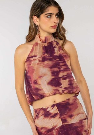 Joven mujer con top de tirantes halter y falda a juego con patrones abstractos en púrpura y beige, mirando hacia un lado.