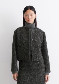 Gekürzte Jacke aus dunklem, strukturiertem Stoff mit Fischgrätenmuster, mit rundem Ausschnitt, zwei frontalen Taschen und Knopfverschlüssen.