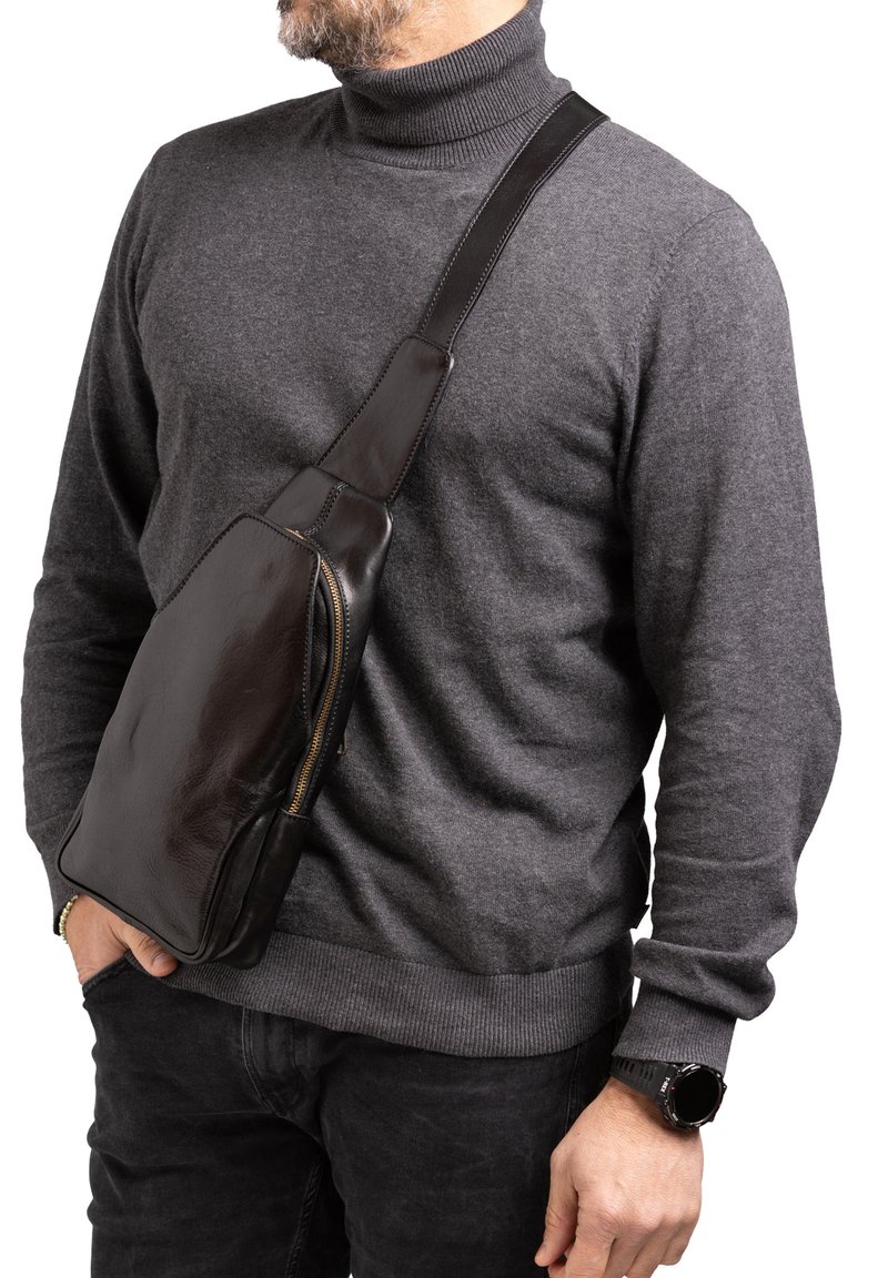 Borsa a tracolla in pelle marrone con texture liscia, chiusura con zip e design slim e angolato. Indossata sopra un dolcevita grigio.