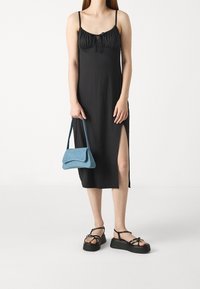 Musta midi-mekko säädettävillä spagettiolkaimilla, jossa on rypistetty yläosa ja sivuaukko. Yhdistettynä siniseen teksturoituun olkalaukkuun ja mustiin korkeatömmöisiin sandaaleihin.
