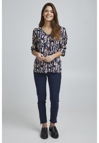 Blusa a righe blu navy e crema con maniche a sbuffo, abbinata a pantaloni slim-fit blu navy scuro e scarpe slip-on nere.