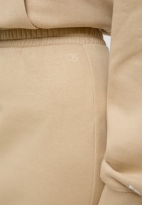Beige joggingbroek met een zachte textuur, elastische tailleband en een klein wit "QS" logo aan de linkerkant.