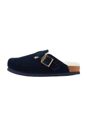 Zueco negro de ante con hebilla dorada, suela de corcho y suave forro interior blanco visible en el talón.